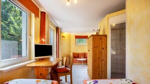Una habitación con dos camas, un escritorio con computadora, una silla, una mesita y un armario.