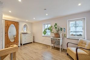 Quarto com piso de madeira, penteadeira branca, espelho, cadeira e planta em vaso.