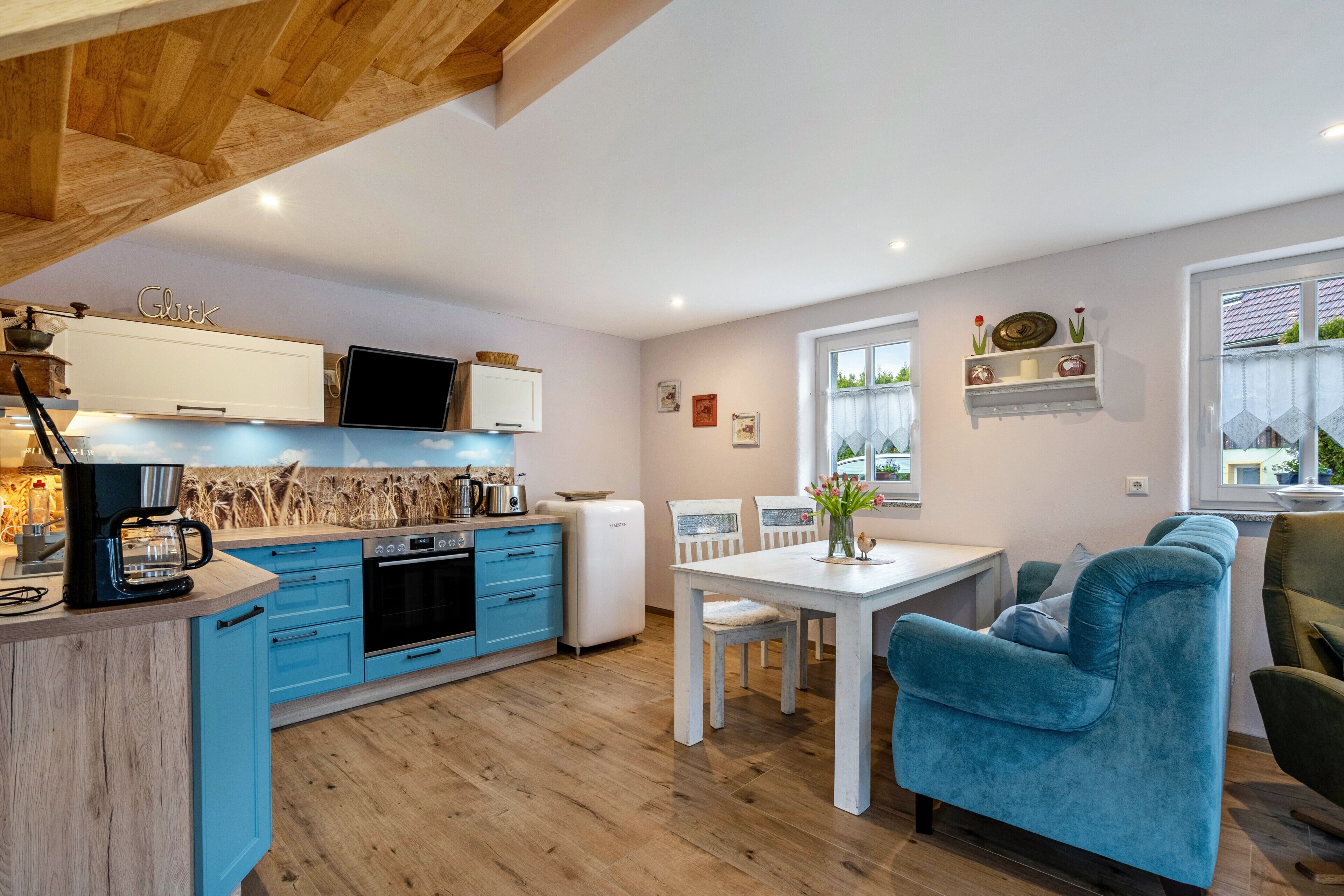 Een moderne keuken met blauwe kasten, een witte eettafel en een blauwe bank.
