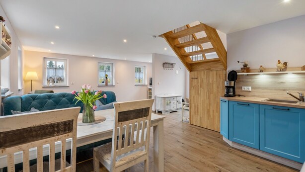 Une cuisine moderne avec des meubles en bois, un coin repas avec une table et des chaises, et une chambre à coucher située en mezzanine avec un plafond en pente.