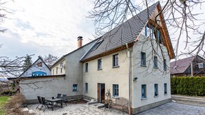 Une maison à deux étages, avec un toit en tuiles, une porte d’entrée et un petit patio équipé d’une table et de chaises.