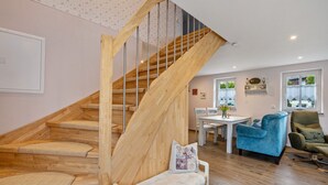 Un escalier en bois avec un banc en bas, une table à manger avec des chaises, et un fauteuil bleu dans un salon doté d’un plancher en bois.