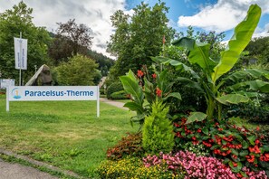 Een bord met Paracelsus-Thermo, omringd door weelderige begroeiing en bloeiende planten.