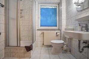 A bathroom with a shower, toilet, sink, and a window with blinds. - Apartment 'Haus Hügel  - Wohnung 4' with Balcony and Wi-Fi (Binz)
