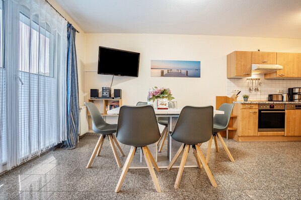 A modern kitchen with a flat-screen TV, wooden cabinets, and a dining area with chairs.