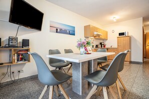A modern kitchen with a flat-screen TV, wooden cabinets, and a dining area with a white table and black chairs. - Apartment 'Haus Hügel  - Wohnung 4' with Balcony and Wi-Fi (Binz)