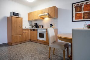 Une cuisine compacte dotée de meubles en bois, d’un four à micro-ondes, d’une cuisinière et d’un coin repas avec une chaise et une table.
