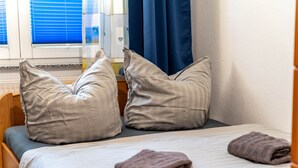 Een bed met twee kussens, een opgevouwen handdoek en een raam met blauwe gordijnen.