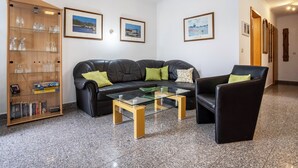 Een woonkamer met een zwarte leren bank, een glazen salontafel, een boekenkast en ingelijste foto's aan de muur.