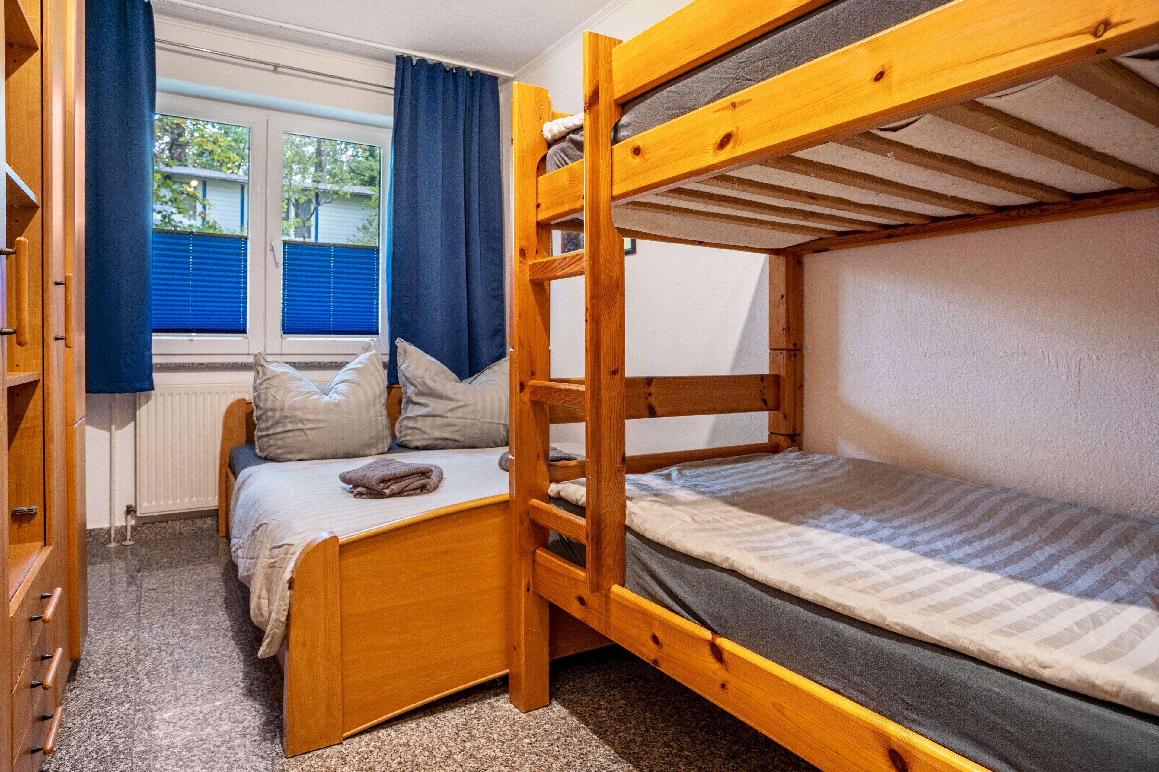 Ein Schlafraum mit Etagenbett, Fenster, Vorhängen und einer Holzkommode.