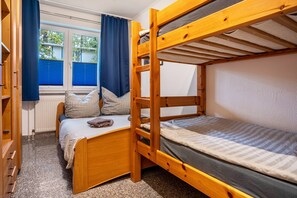 Une chambre avec un lit superposé, une fenêtre, des rideaux et une commode en bois.