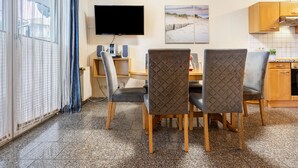 Un comedor con televisor, altavoces y una imagen con motivos playeros en la pared.