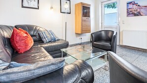 Una sala de estar moderna con un sofá de cuero, una mesa de centro de vidrio, un sillón negro y un mueble de madera.