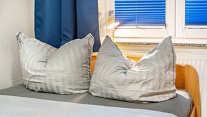 Una cama con dos almohadas, una ventana con persianas y una lámpara en una mesita de noche.