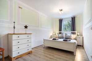 Une chambre à coucher comprenant un lit, une commode, des tables de chevet et une fenêtre avec des rideaux.