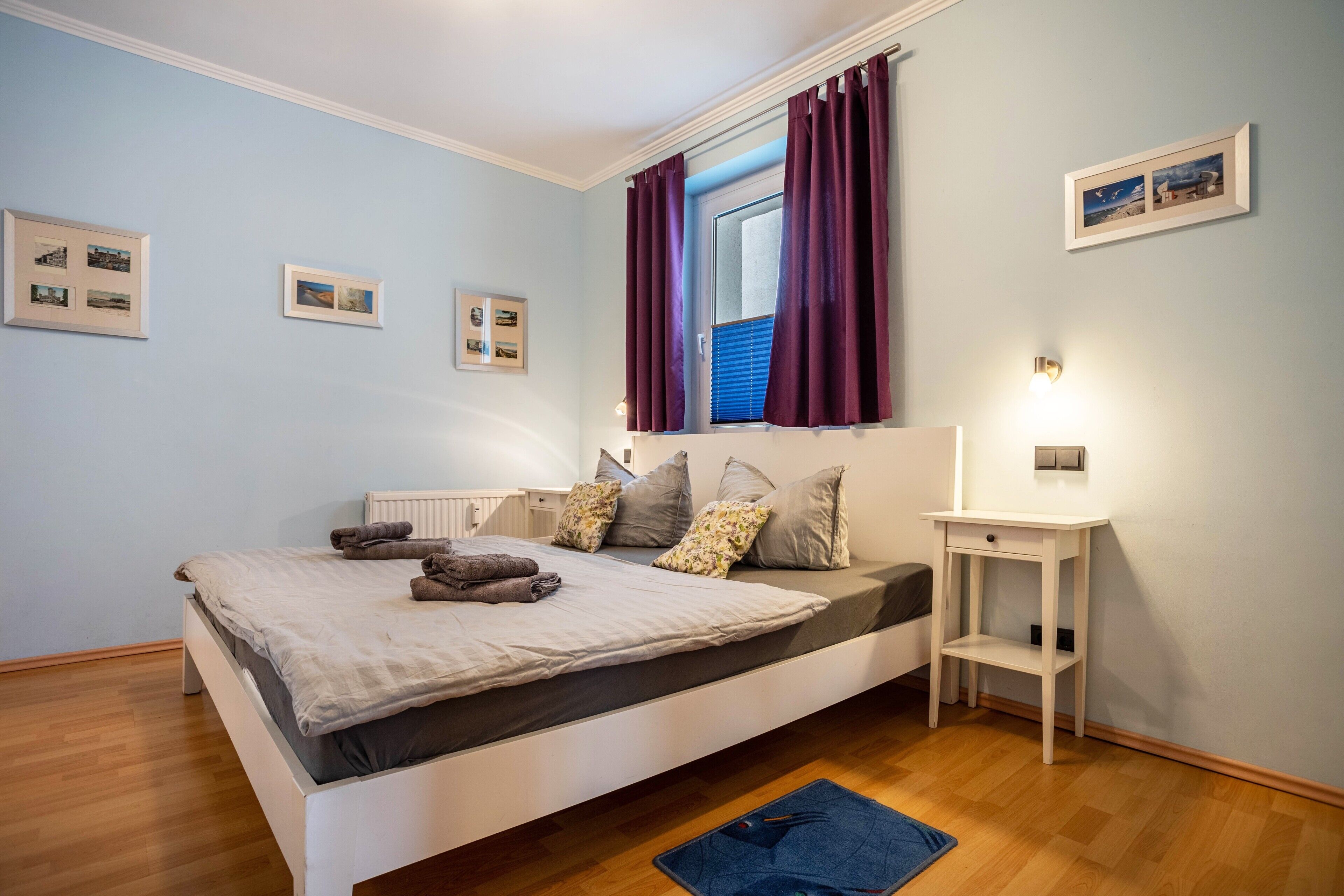 Ein Schlafzimmer mit Bett, Nachttisch, Fenster mit Vorhängen und Wandleuchten.