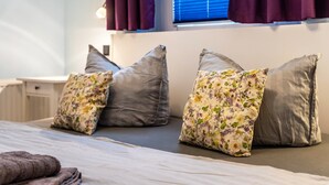A neatly made bed with pillows, a bedside table, and a window with curtains. - Apartment 'Haus Frohsinn - Wohnung 6' with Wi-Fi (Binz)
