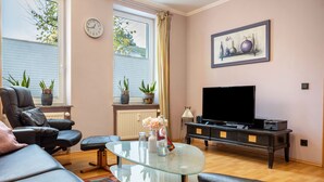 A living room with a leather sofa, a glass coffee table, a TV on a black stand, and potted plants. - Apartment 'Haus Frohsinn - Wohnung 6' with Wi-Fi (Binz)