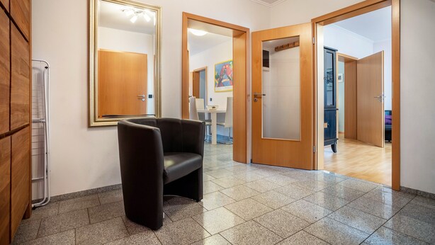 A hallway with a black leather chair, wooden doors, a white radiator, and a tiled floor. - Apartment 'Haus Frohsinn - Wohnung 6' with Wi-Fi (Binz)
