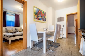 A modern room with a bed, a dining table with chairs, a painting on the wall, and a kitchen area.