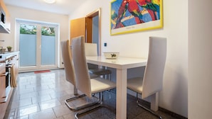 A dining area with a white table, four chairs, a painting of colorful birds, and a view of a sliding door leading to a balcony. - Apartment 'Haus Frohsinn - Wohnung 6' with Wi-Fi (Binz)