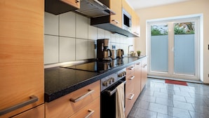 A modern kitchen with a black countertop, stainless steel appliances, wooden cabinets, and a sliding glass door leading to a balcony. - Apartment 'Haus Frohsinn - Wohnung 6' with Wi-Fi (Binz)