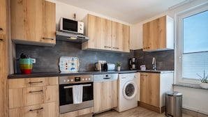 Une cuisine moderne dotée de meubles en bois, d’un four à micro-ondes, d’un grille-pain, d’une machine à café, d’un lave-linge et d’une poubelle.