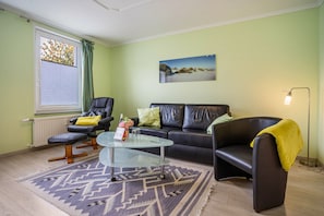 A living room with a glass coffee table, a sofa, a chair, a floor lamp, and a window with blinds.