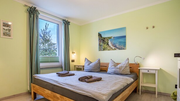 Une chambre à coucher avec un lit en bois, une table de chevet, une commode, un tableau et une fenêtre avec des rideaux.