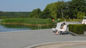 Un banc placé près d’un plan d’eau, avec un sentier, des arbres et une vue lointaine sur une colline.