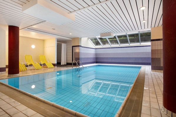 An indoor swimming pool with tiled walls, a skylight, and yellow lounge chairs.