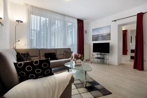A modern living room with a sofa, a glass coffee table, a flat-screen TV, and a painting on the wall.