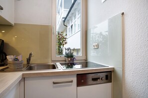 A kitchen with a Bosch dishwasher, a window with a view of a building, and a plant on the windowsill.