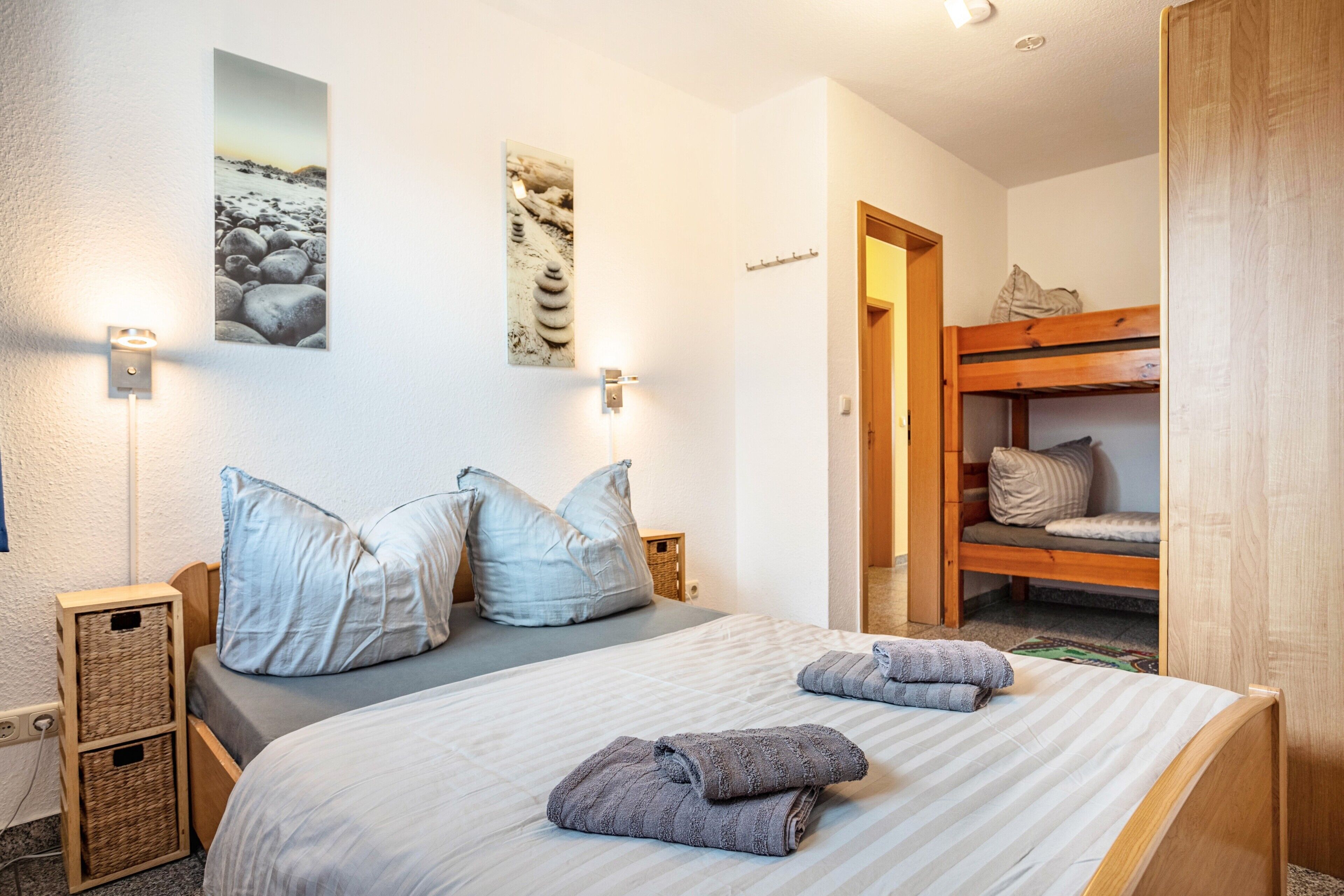 Ein Schlafzimmer mit einem Bett, Kissen, einem Holzbett mit Etagen und Wandleuchten sowie einem gerahmten Bild.