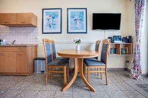 A dining area with a round table, four chairs, a vase with flowers, a TV, and a bookshelf with books. - Apartment 'Haus Frohsinn - Wohnung 3' with Balcony and Wi-Fi (Binz)