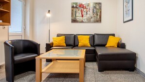 Una sala de estar con un sofá de cuero negro, una mesa de centro de vidrio, un sillón negro y un cuadro en la pared.