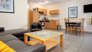 Un espacio habitable compacto con sofá, una mesita, kitchenette y zona de comedor con sillas.