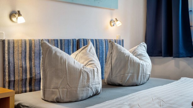 Habitación de hotel con cabecera a rayas, dos almohadas, una cama y luces fijadas a la pared.