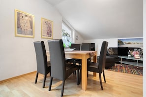 Un coin repas avec une table en bois et des chaises noires, un canapé et deux œuvres d’art encadrées accrochées au mur.