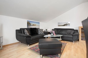 Un salon moderne avec deux canapés noirs, une petite table basse et un tapis aux couleurs vives.