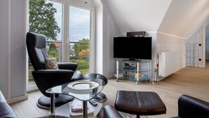 A modern living room with a glass coffee table, black leather sofa, and a flat-screen TV. - Apartment 'Bäckerhus - Ferienwohnung 4' with Private Terrace, Shared Garden and Wi-Fi (Wiek)