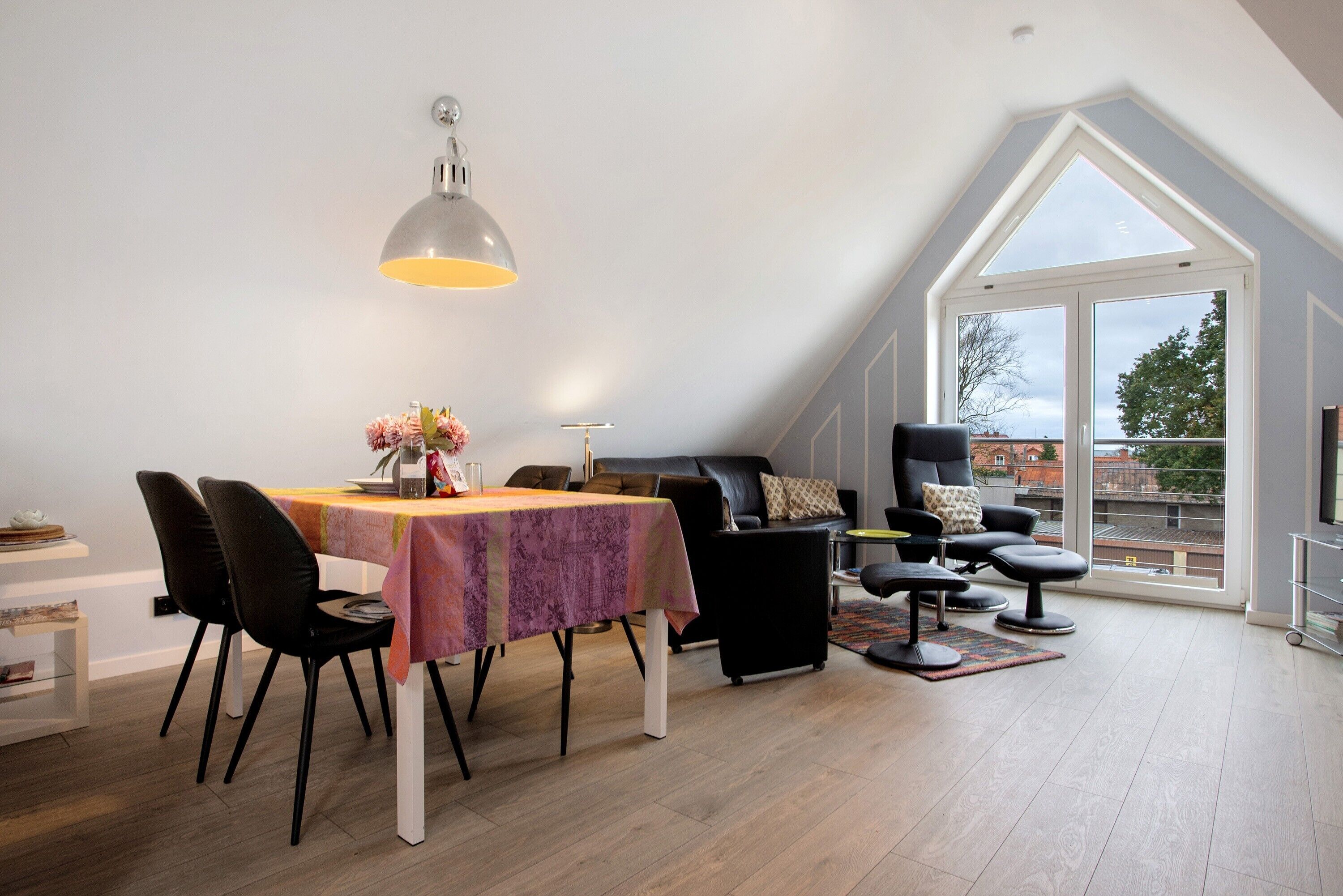 A dining area with a table, chairs, a pendant light, and a view through a large window.
