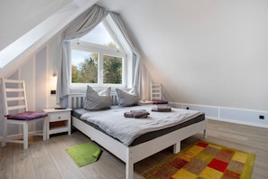 A bedroom with a sloped ceiling, a bed with pillows, a nightstand, a chair, a window, and a colorful rug. - Apartment 'Bäckerhus - Ferienwohnung 4' with Private Terrace, Shared Garden and Wi-Fi (Wiek)