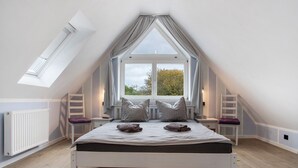 A bedroom with a sloped ceiling, a skylight, a bed with pillows, a window, and a radiator. - Apartment 'Bäckerhus - Ferienwohnung 4' with Private Terrace, Shared Garden and Wi-Fi (Wiek)