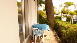 Eine Terrasse mit Tisch und Stühlen, ein Blumentopf mit Blumen und ein Hecken.