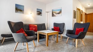 Ein modernes Wohnzimmer mit einer Couch, zwei Sesseln, einem Couchtisch und Kunstwerken an den Wänden.