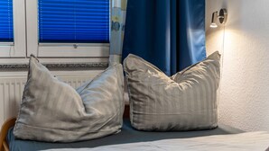 Ein Bett mit zwei Kissen, einer Wandleuchte und einem Fenster mit Jalousien.