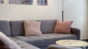 Un canapé gris avec trois coussins, une table basse ronde et un cadre photo fixé au mur.