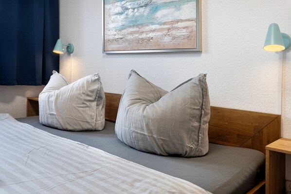 A bed with two pillows, a wall-mounted painting, and two wall lamps.