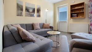 Un salon avec un canapé gris, une table basse ronde et une bibliothèque contenant des objets en verre.